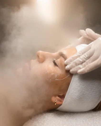 Cliente de olhos fechados com faixa na cabeça recebendo limpeza de pele com vapor
